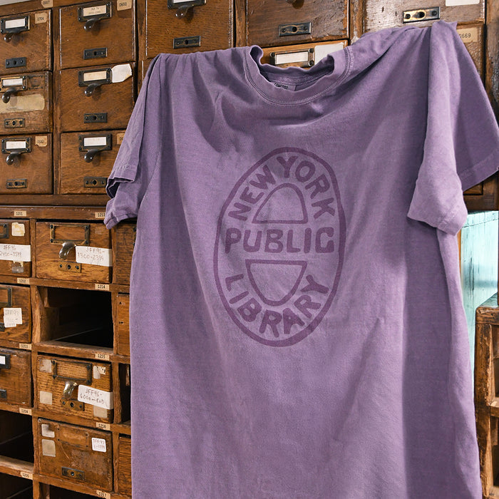 Close-up of purple shirt that features an oval NYPL bookbinding stamp hanging from card catalogs.
