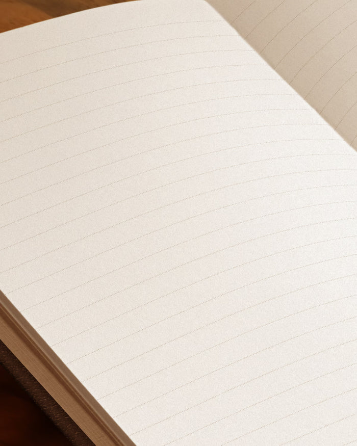 An open lined notebook showing blank, off-white paper with horizontal ruling, photographed close up against a dark brown background.