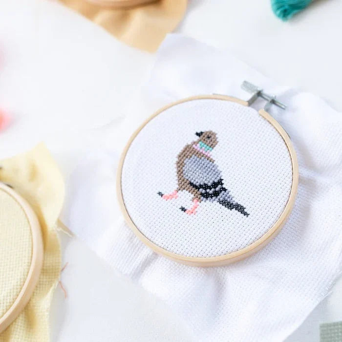 Cross-stitched bird design in an embroidery hoop on a white fabric background