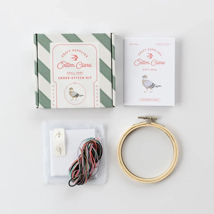 Cross-stitch kit with hoop, thread, and packaging on a white background