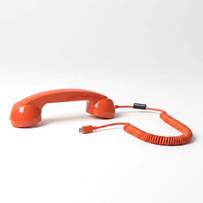 A retro-style orange rotary telephone handset with a coiled orange cord and a USB-C connector, shown on a clean white background.