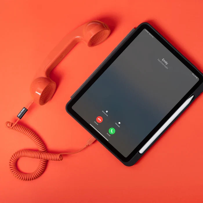 Tablet with phone app on screen next to a red vintage-style phone on an orange background