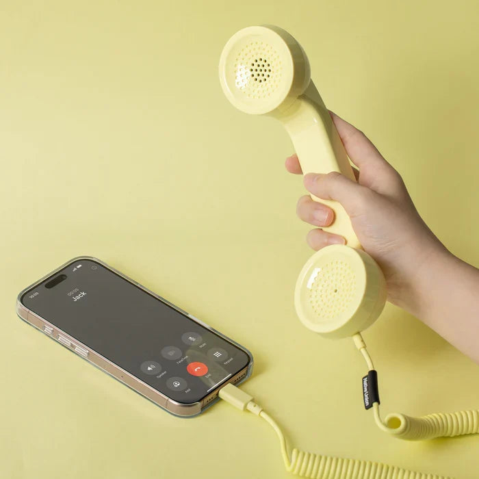 Hand holding a yellow phone receiver connected to a smartphone on a yellow background