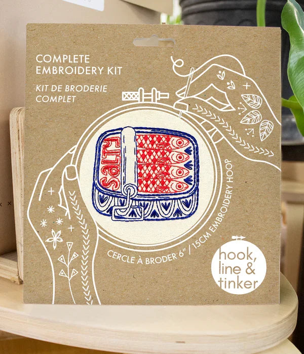 Box for a complete embroidery kit with 'hook, line & tinker' branding on a wooden surface.