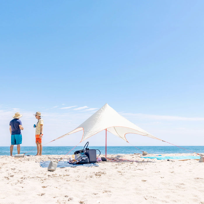 shadecaster 2 sun shade next to the ocean with a bunch of gear in the shade while some guys shoot the breeze