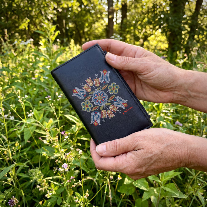 Hand holding a black wallet with floral designs against a natural background