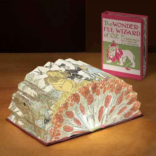Open book with detailed illustrations and a closed book titled 'The Wonderful Wizard of Oz' on a wooden surface.
