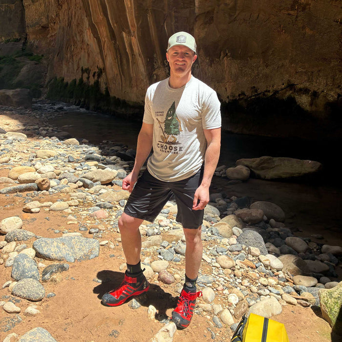 Man standing on a rocky trail wearing hiking shoes and a t-shirt with a graphic design.