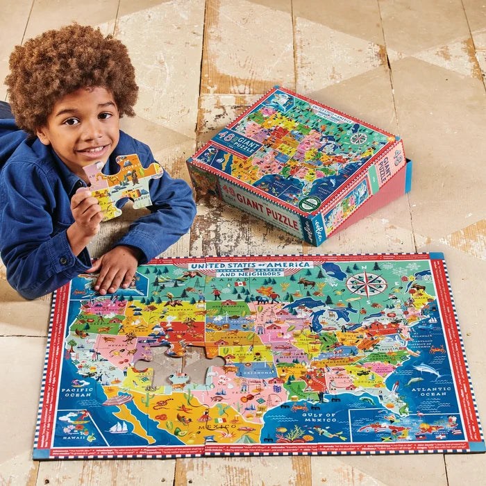 Child with a colorful puzzle of the United States and a matching box on a wooden floor.