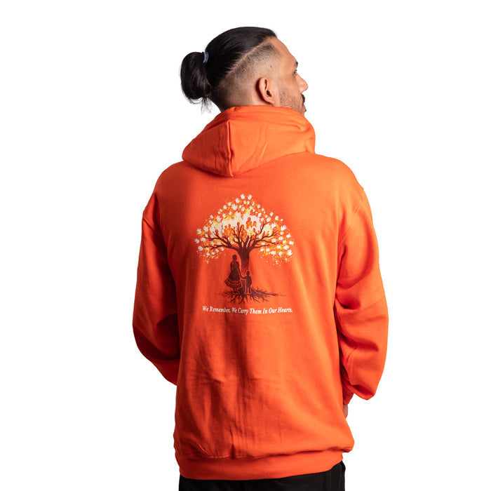 Person wearing an orange hoodie with a tree design on the back, standing against a white background