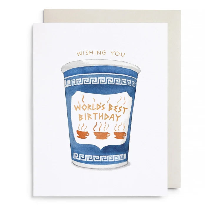 A white greeting card with a watercolor illustration of a blue coffee cup and the words 'WORLD'S BEST BIRTHDAY' in gold, shown with a light beige envelope behind it on a white background.