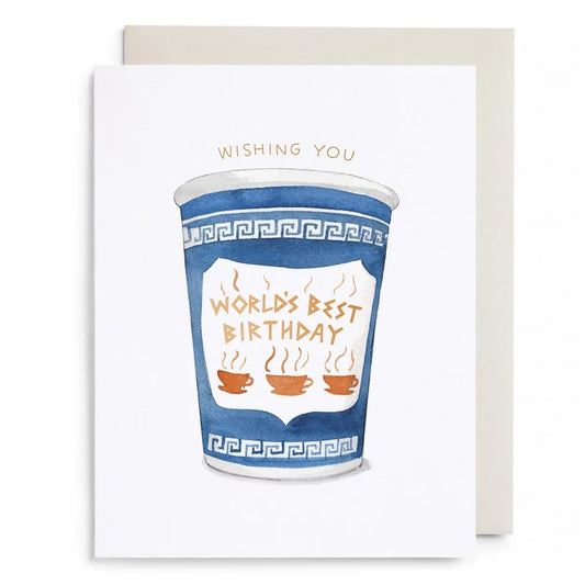 A white greeting card with a watercolor illustration of a blue coffee cup and the words 'WORLD'S BEST BIRTHDAY' in gold, shown with a light beige envelope behind it on a white background.