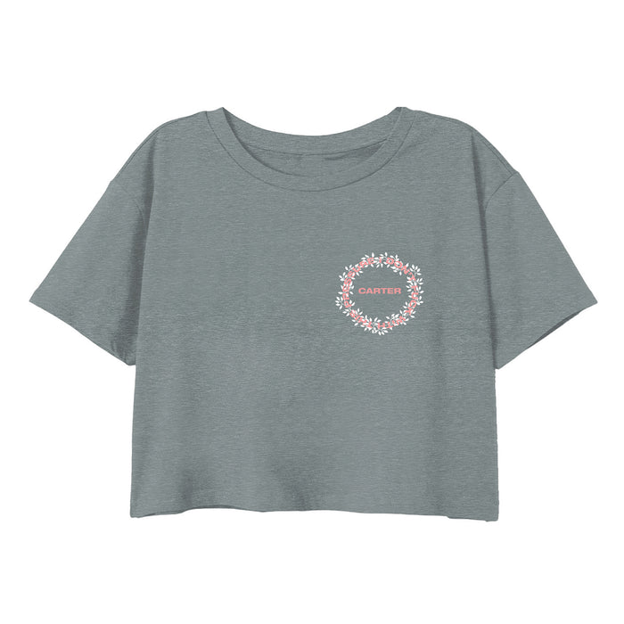 A gray cropped T-shirt from Tyler Carter features a small circular floral wreath on the left chest with CARTER in white capital letters inside the wreath.